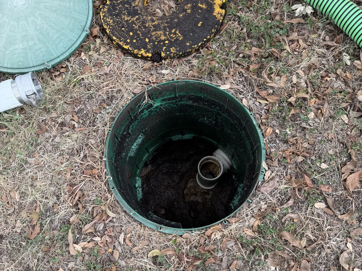 An open septic riser with the lid set aside during a tank inspection