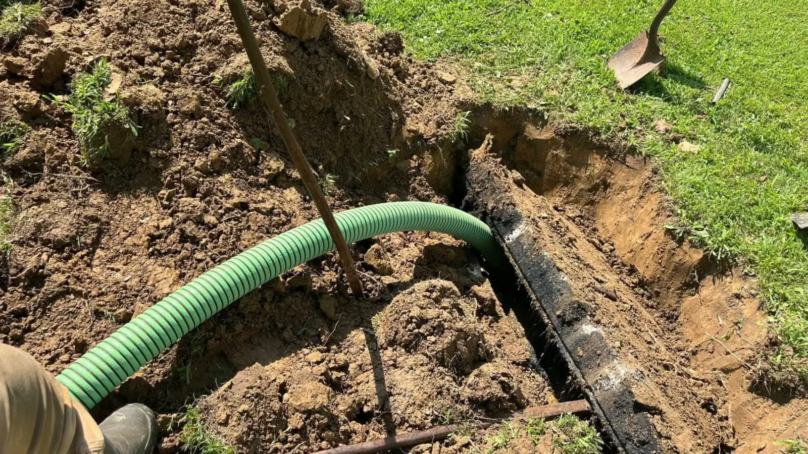 Septic tank pumping with the suction hose run into a dug-out tank opening in a grassy yard