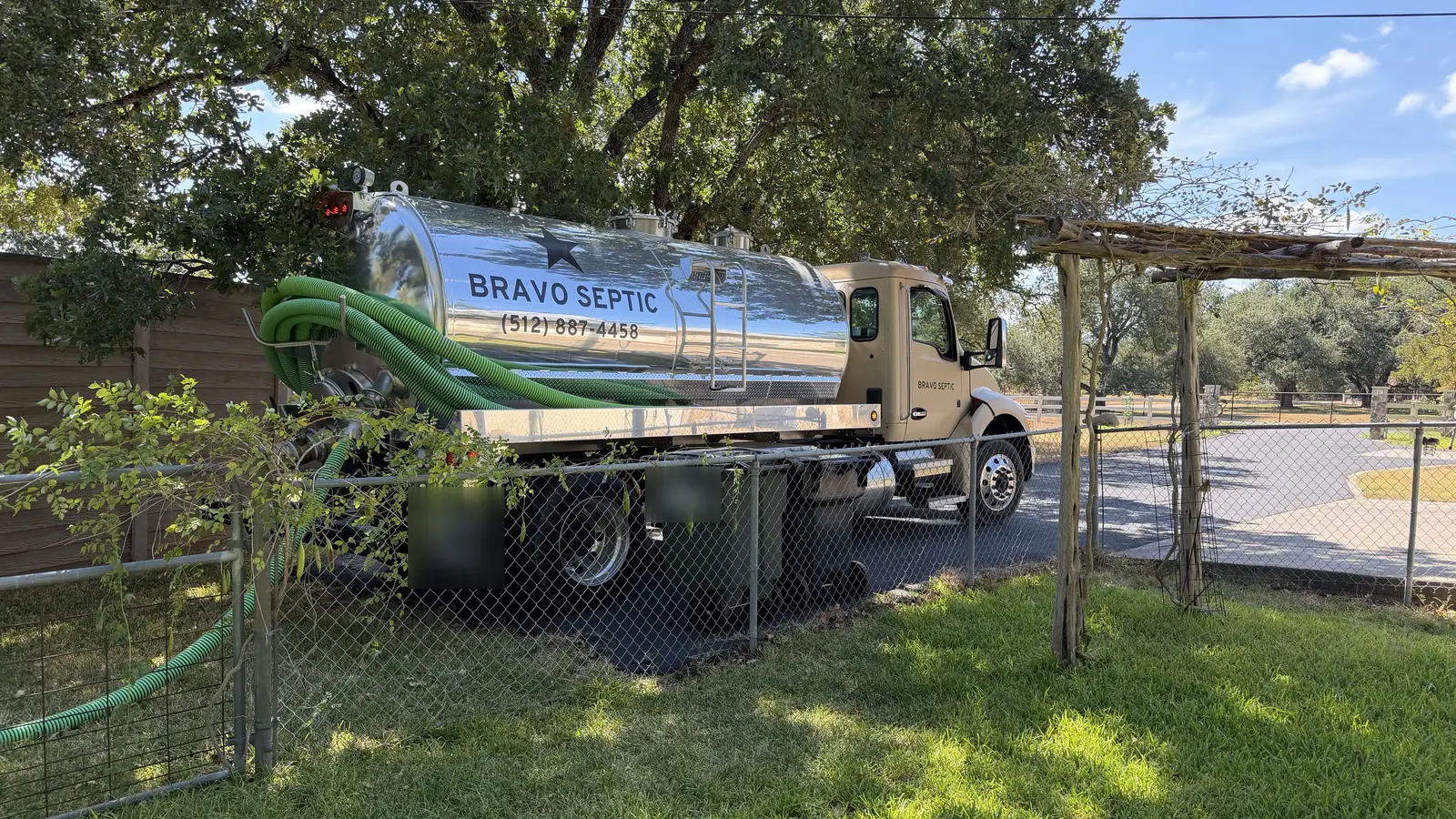 The Bravo Septic pump truck that serves Jarrell, parked under live oaks with its hose run over a fence
