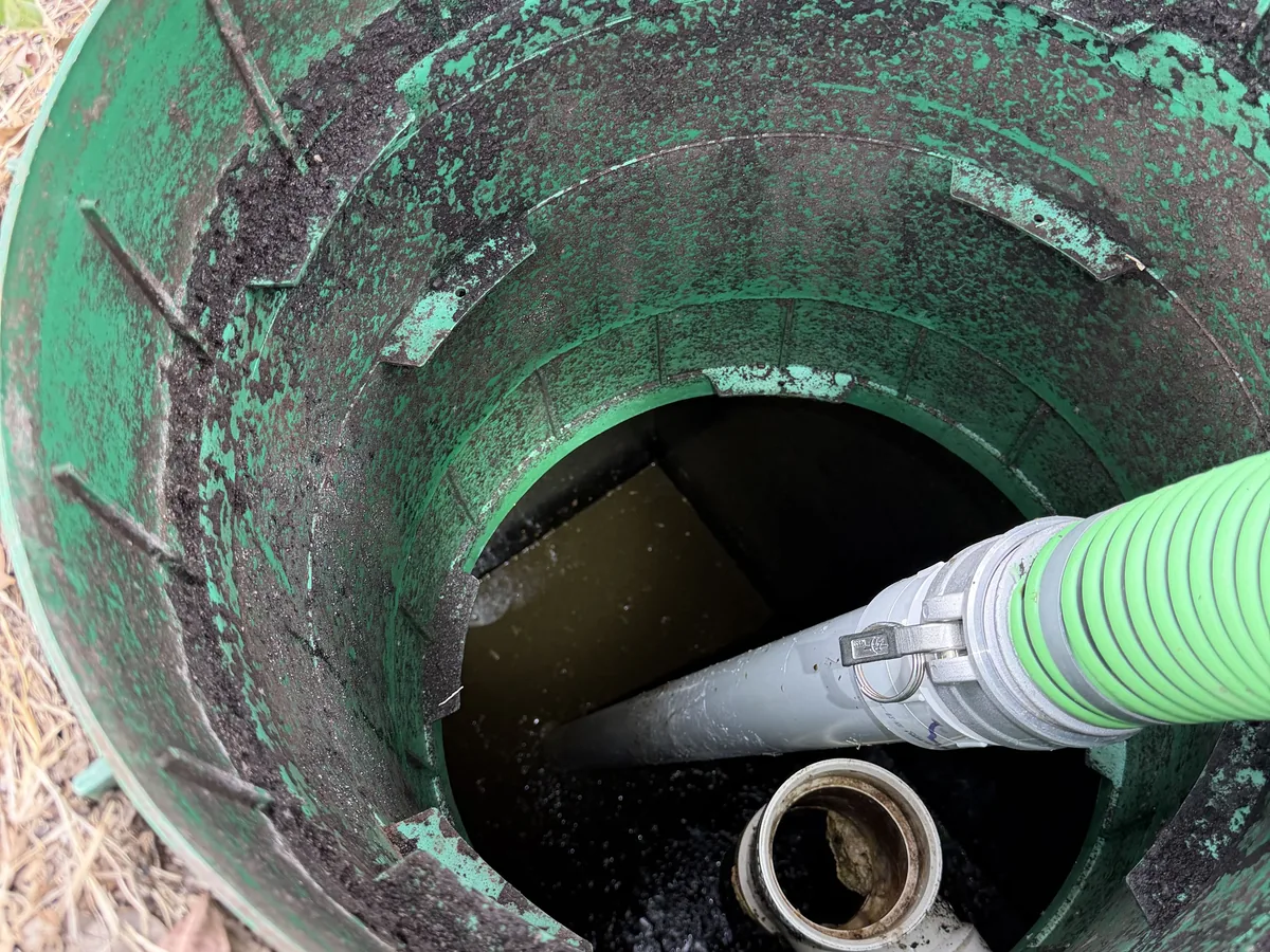 The suction hose lowered into a green septic riser during pumping