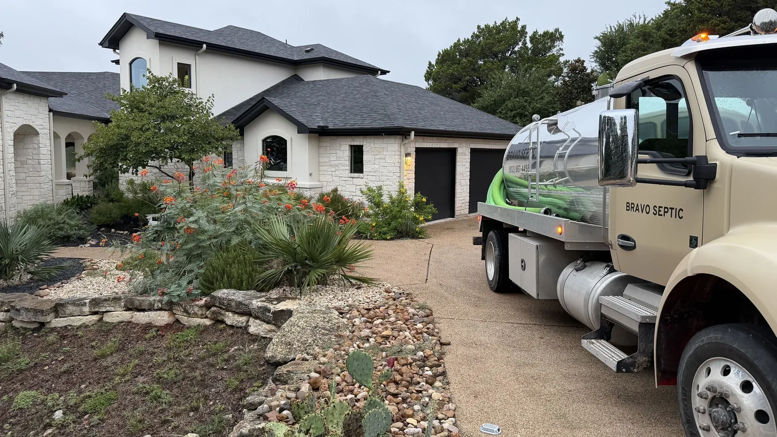 A Hill Country home with a stone-edged rock garden and the Bravo Septic pump truck in the driveway